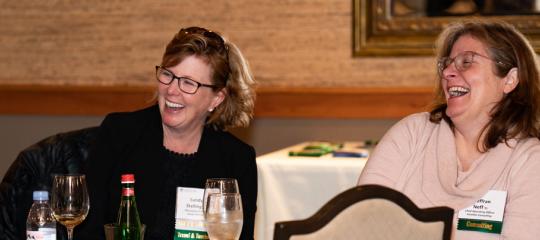 Two alumnae sitting at a table and laughing