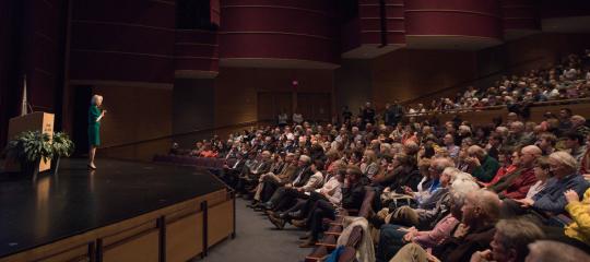 Woman standing on a stage speaking to an audience