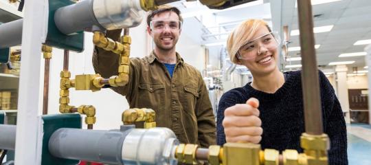 Students standing and smiling behind piping