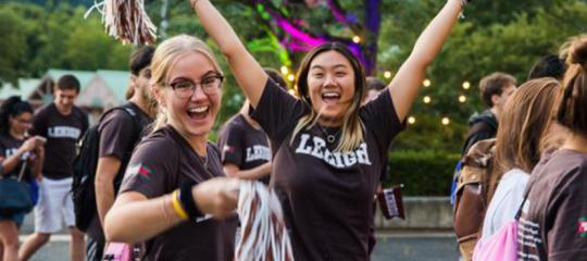Two female Lehigh University students with pom poms and brown Lehigh gear on cheer in excitement
