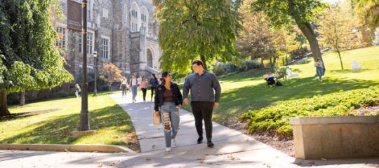 Two people smiling and walking down a concrete pathway on campus