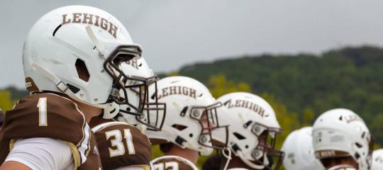 A row of football players line up for a view of their profiles and sides of their white helmets with the numbers on their shoulders facing the camera..