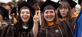 Two female graduates smiling and dressed in their commencement regalia